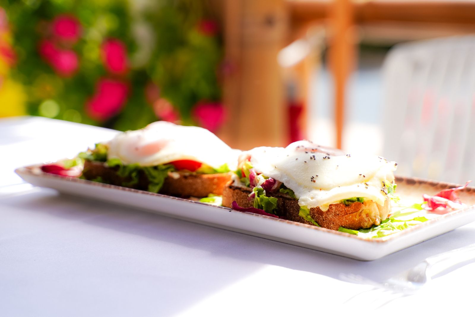 Two open sandwiches topped with poached eggs and greens on a white table