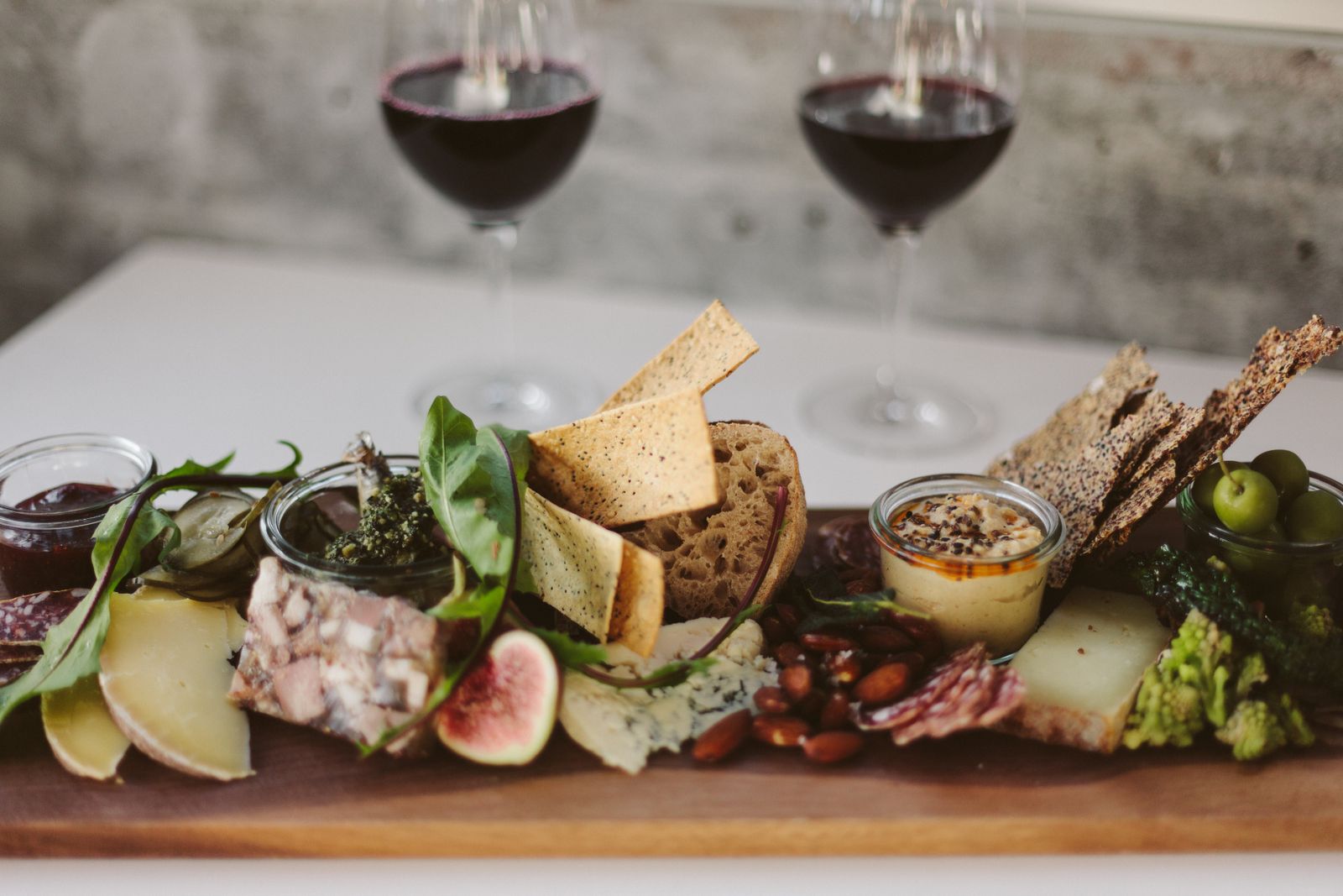 A board of cheeses, cured meats, figs and crackers beside two glasses of red wine