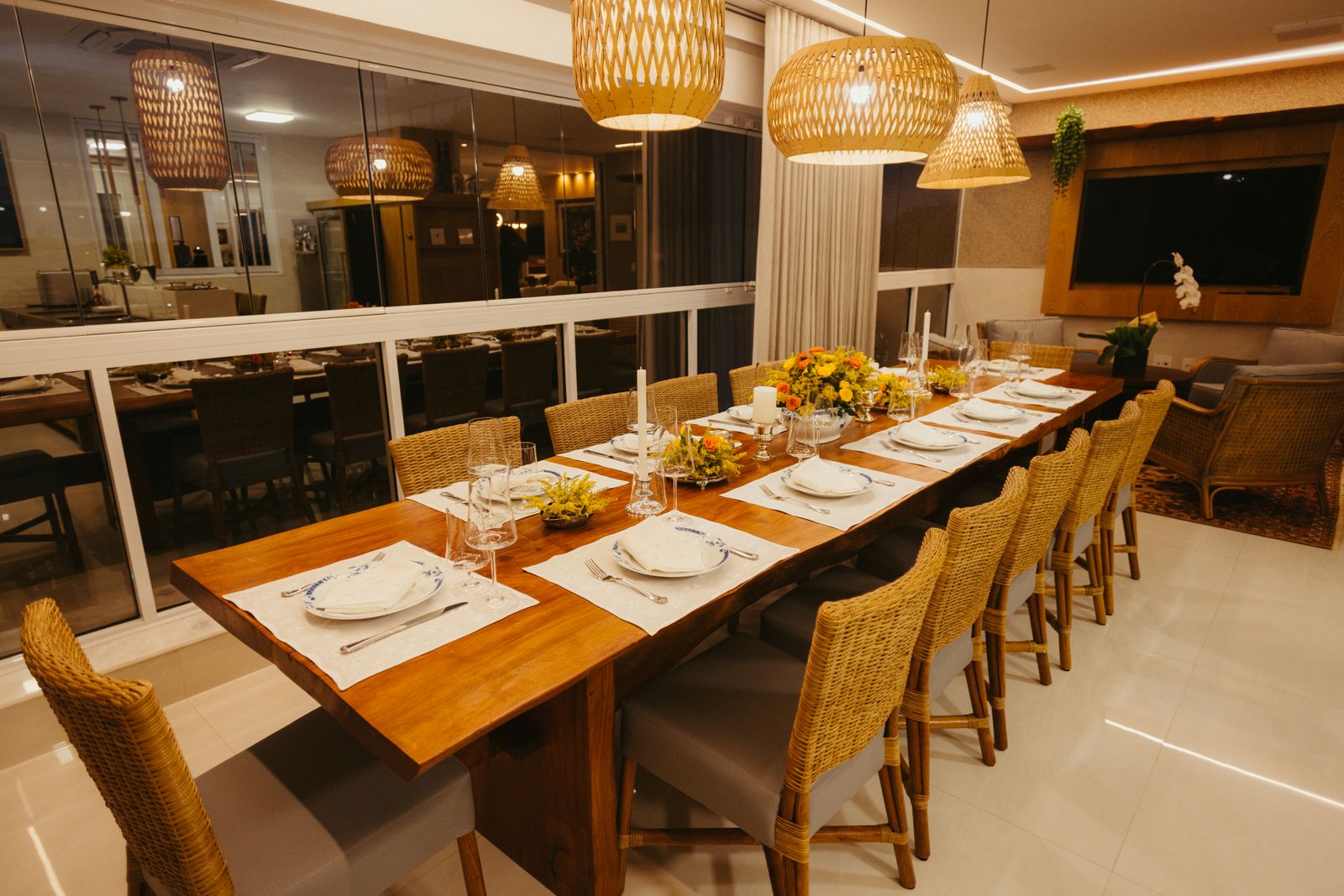 A long wooden table set for a dinner party, with woven chairs and hanging lamps