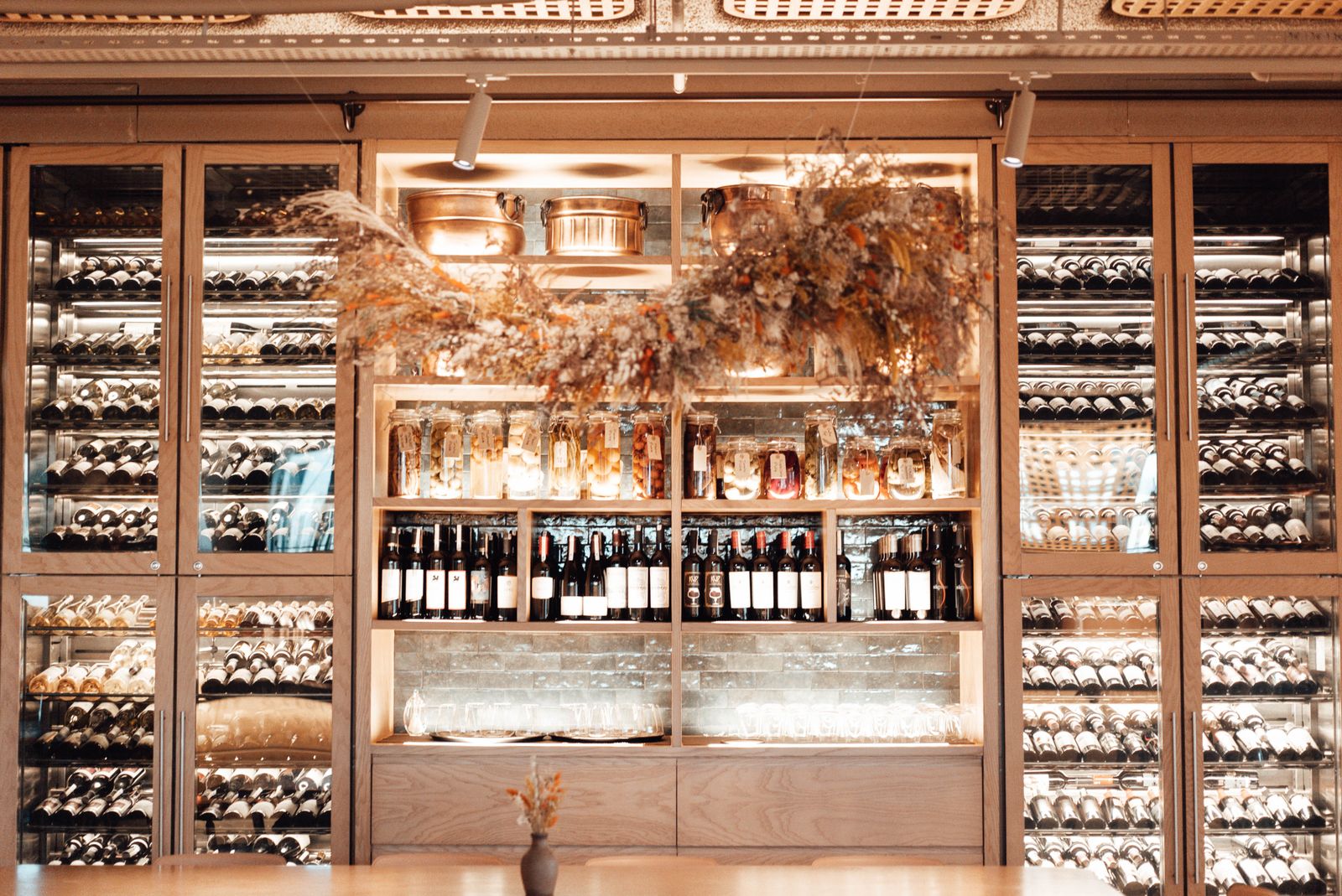 A wall of wine bottles on lit wooden shelves behind a bar